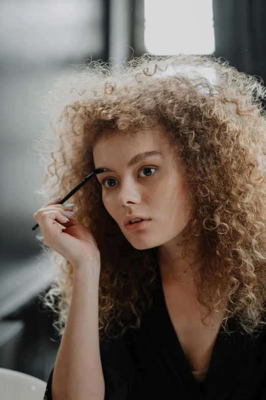 a woman sitting at a table with a cup of coffee, by Adam Marczyński, trending on pexels, renaissance, her face framed with curls, putting makeup on, black eyeliner, frizzy hair