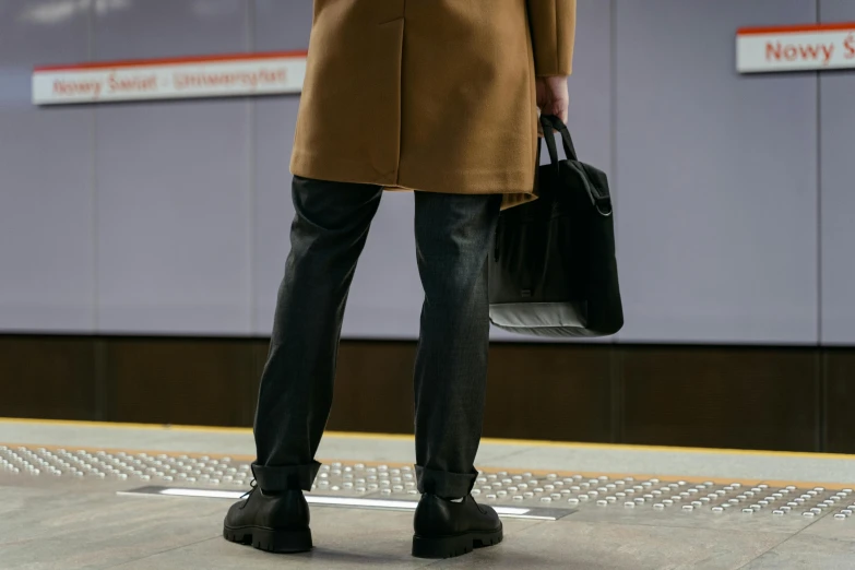 a man in a brown coat holding a black bag, unsplash, hyperrealism, platform boots, subways, dezeen, animation