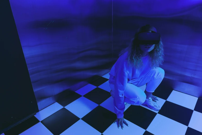 a woman sitting on a black and white checkered floor, a hologram, unsplash contest winner, interactive art, wearing vr goggles, blue room, indie video game horror, looking down