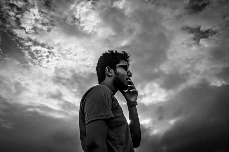 a man talking on a cell phone under a cloudy sky, a black and white photo, by Jitish Kallat, pexels, romanticism, thinking pose, a portrait of rahul kohli, portait photo profile picture, during golden hour