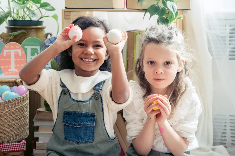 a couple of young girls sitting next to each other, inspired by Elsa Beskow, pexels contest winner, process art, holding in the hands easter eggs, activity play centre, all looking at camera, diverse ages