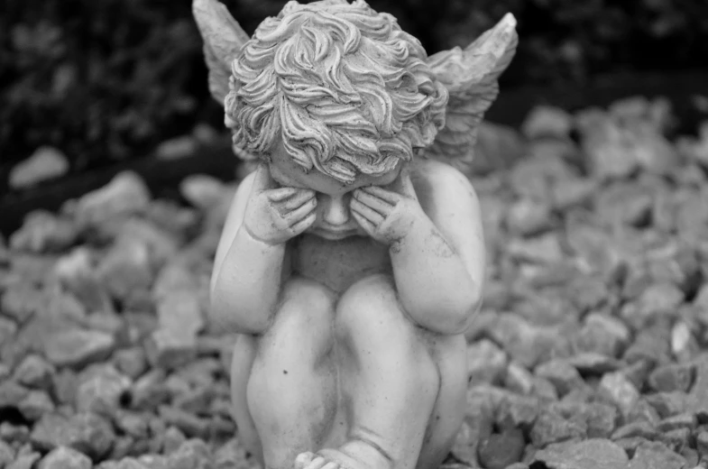 a statue of an angel sitting on a pile of rocks, pexels, fine art, is totally sad and cries, monochrome:-2, cherub, pouting