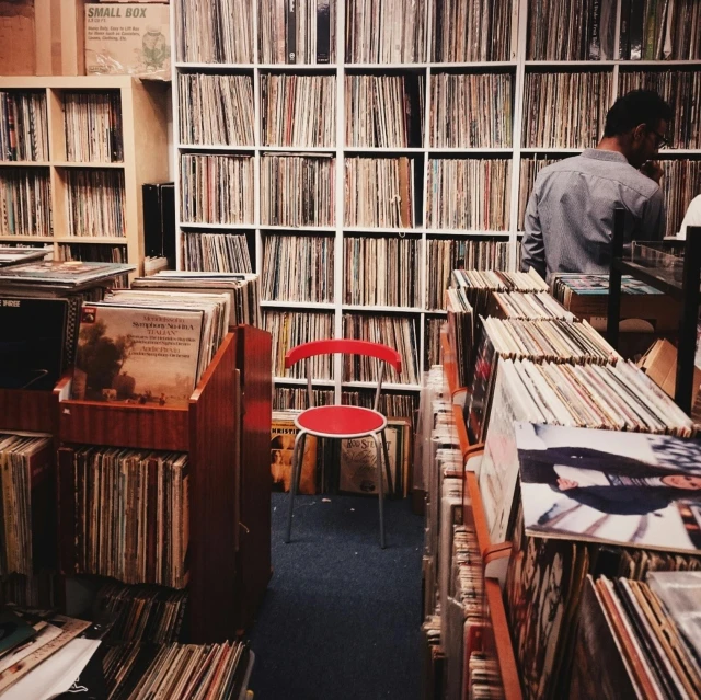 a man standing in a room filled with lots of records, an album cover, by Niko Henrichon, trending on unsplash, sitting on a store shelf, paris 1982, wheres wally, from the distance