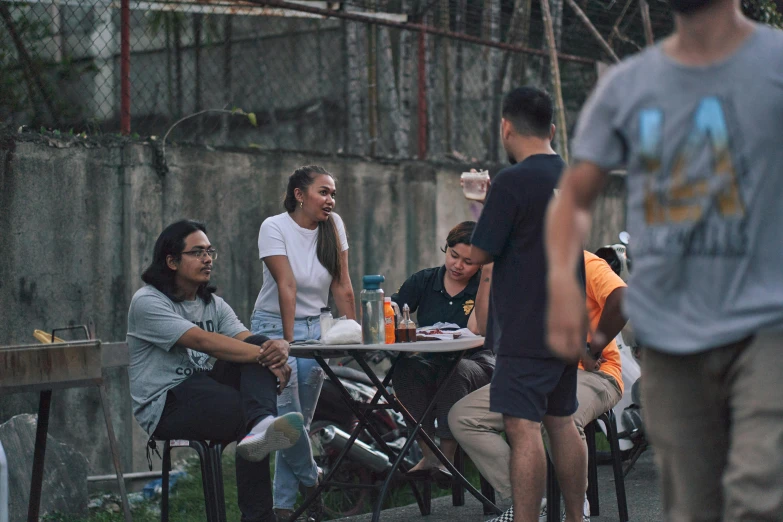 a group of people sitting at a table outside, happening, manila, chillhop, neighborhood, walking down