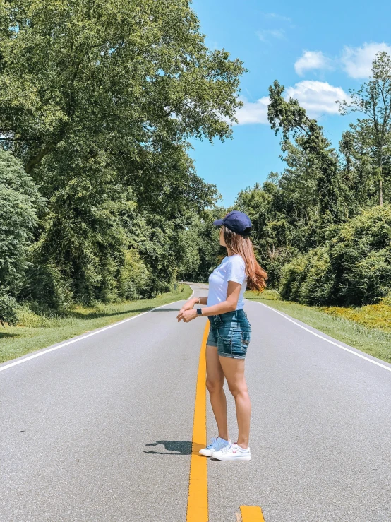 a woman standing in the middle of a road, wearing shorts and t shirt, profile image, landscape photo