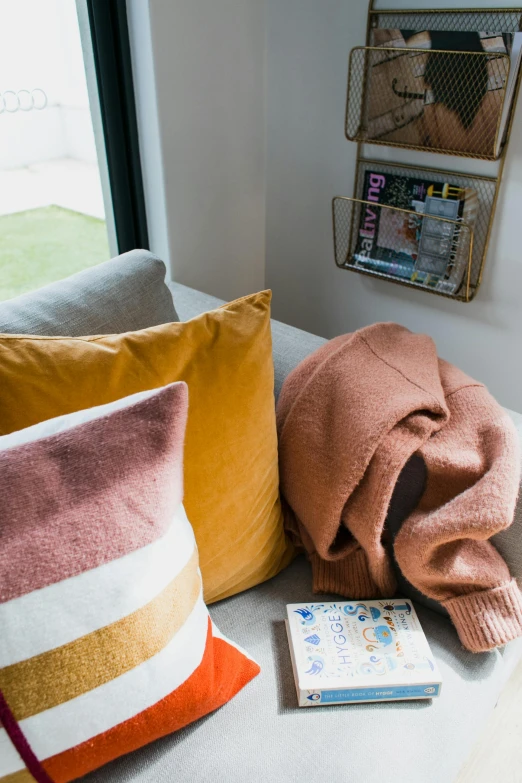 a couple of pillows sitting on top of a white couch, a picture, filled with books, warm color clothes, toned orange and pastel pink, detailed product image