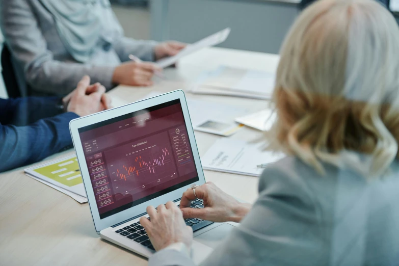 a group of people sitting around a table with laptops, a digital rendering, by Emma Andijewska, trending on unsplash, displaying stock charts, maths, paul barson, mid shot photo