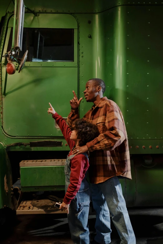 a man and a child standing in front of a green truck, by Dan Frazier, pexels contest winner, train far, raising an arm, ( ( dark skin ) ), ( ( theatrical ) )