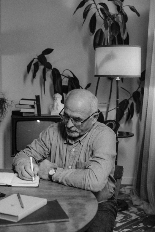 a man sitting at a table writing on a piece of paper, by Edward Avedisian, at home, digital image, arthur clarke, ingmar bergman