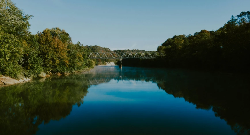 a body of water surrounded by trees and a bridge, blue sky, great river, thomas river, atmospheric cool colorgrade