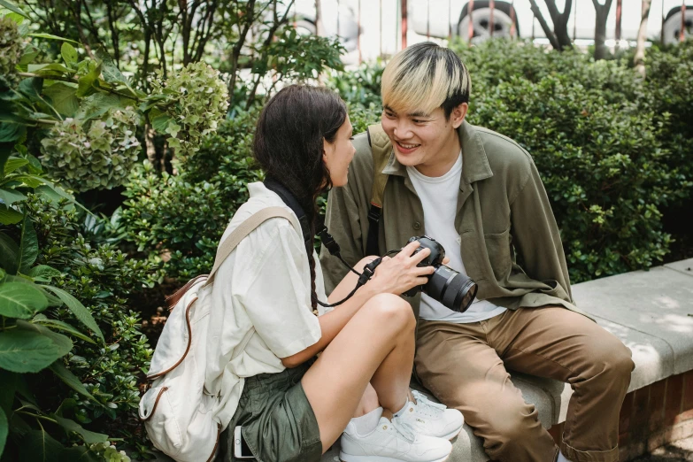 a man and woman sitting next to each other on a bench, a picture, pexels contest winner, holding a dslr camera, asian man, with ivy, flirting smiling