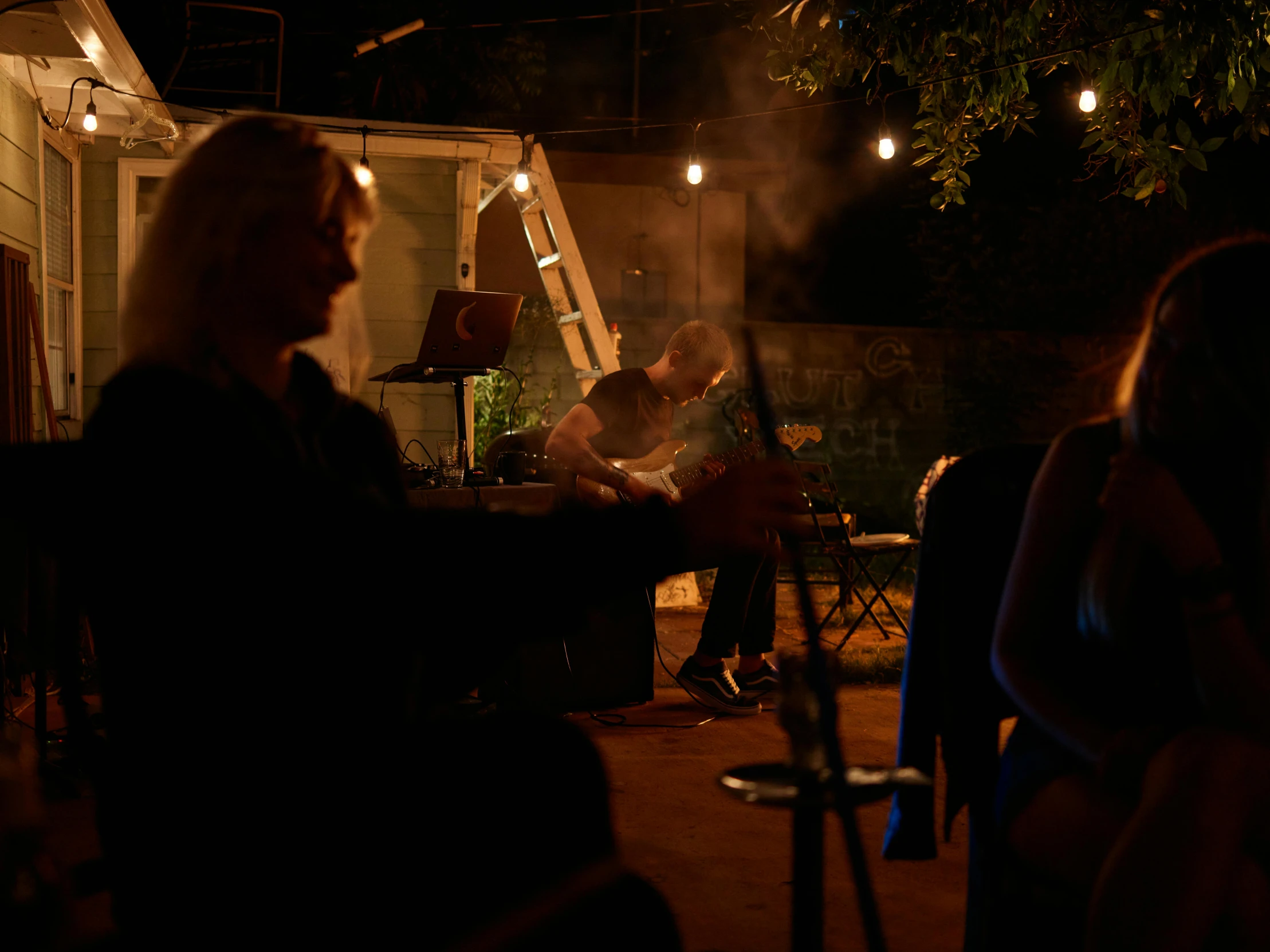 a group of people sitting outside at night, behind the scenes, music being played, profile image, smoky