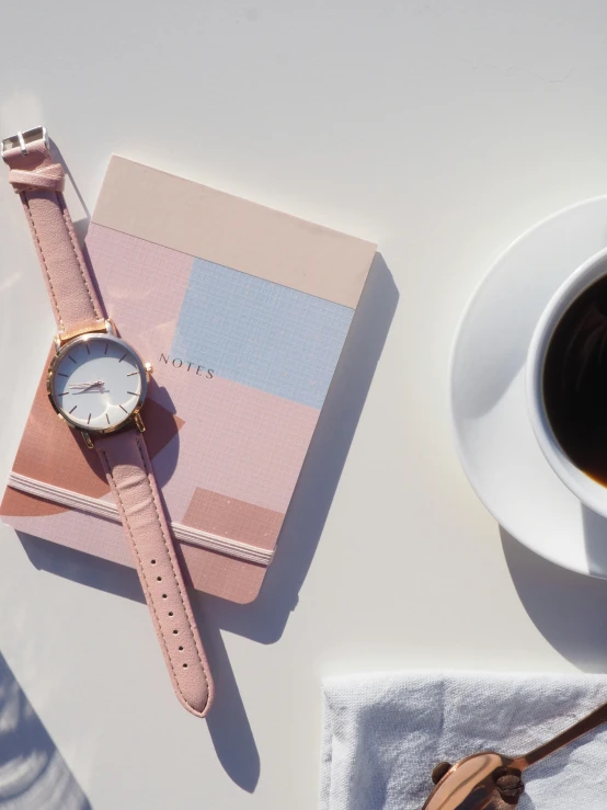 a cup of coffee and a watch on a table, inspired by Emma Andijewska, happening, light pink, organized, profile image, close-up from above