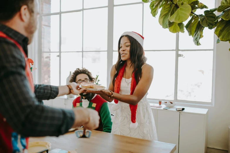 a group of people standing around a table, by Emma Andijewska, pexels contest winner, wearing a santa hat, an olive skinned, serving body, thumbnail