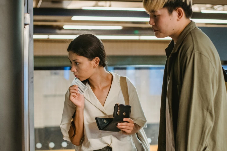 a man and a woman standing next to each other, pexels contest winner, hyperrealism, in a subway, young asian woman, holding a leather purse, inspect in inventory image