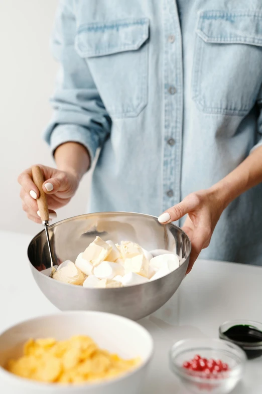 a woman mixing ingredients in a bowl on a table, by Winona Nelson, marshmallows, stainless steal, loosely cropped, square