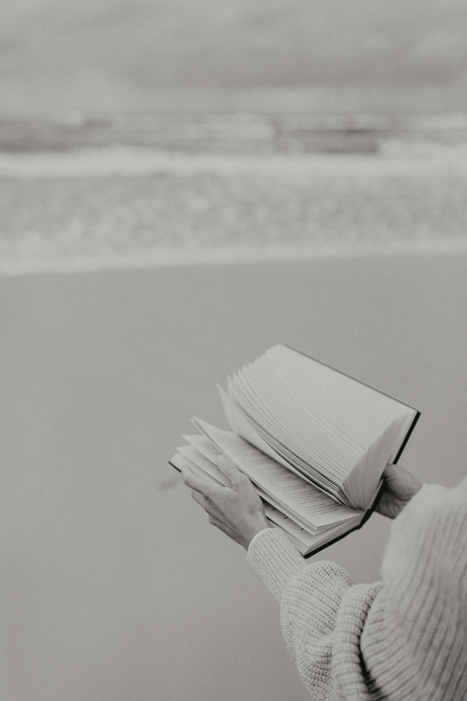 a person standing on a beach holding a book, a black and white photo, unsplash, kaoru mori, without text, seaside, hands