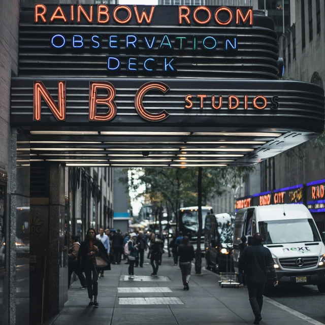 a large neon sign on the side of a building, trending on unsplash, hudson river school, raining rainbow, nbc, inside a grand studio, television show