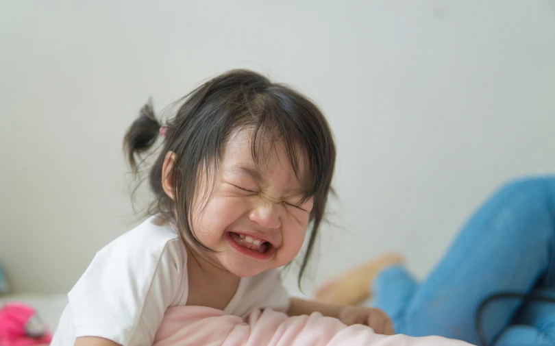 a little girl laying on top of a bed, pexels contest winner, incoherents, screaming and crying, young asian girl, her face flushing and sweat, laughing hysterically