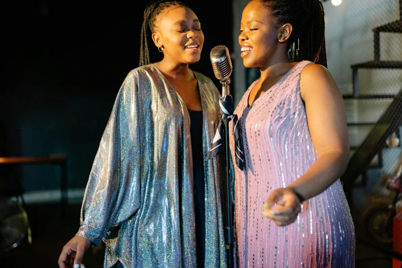 a couple of women standing next to each other on a stage, an album cover, by Ingrida Kadaka, pexels, happening, singing, sparkling, african sybil, thumbnail