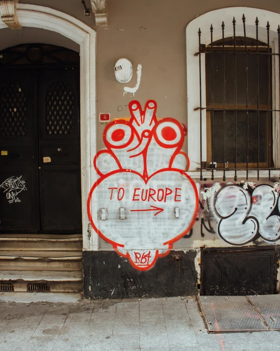 a red and white sign sitting on the side of a building, by Emma Andijewska, pexels contest winner, graffiti, map of europe, lgbtq, doorway, thumbnail