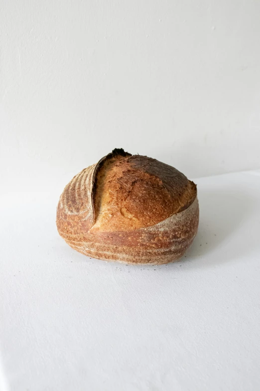 a loaf of bread sitting on top of a white table, round head, heavy grain-s 150, medium, woodfired