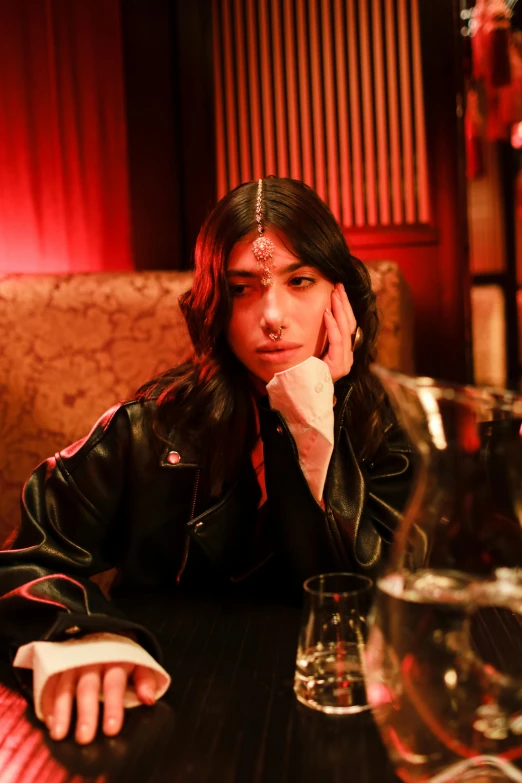 a woman sitting at a table with a glass of wine, an album cover, inspired by Elsa Bleda, trending on pexels, wearing leather jacket, androgynous face, warpaint aesthetic, diner scene