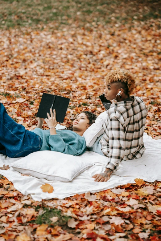 a man and woman laying on a blanket in the leaves, trending on pexels, holding a book, r&b, stylish, ashteroth