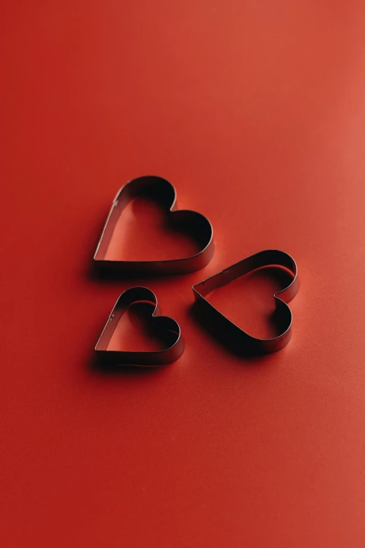 three heart shaped cookie cutters on a red surface, by Jakob Emanuel Handmann, iron, medium, shadows, dwell