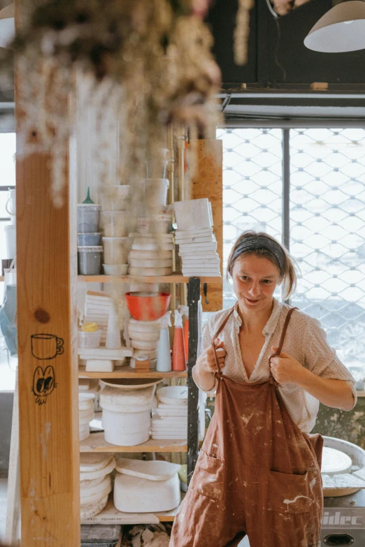 a woman working in a pottery shop, a portrait, by Jessie Algie, trending on unsplash, white waist apron and undershirt, seaside, hanging, ochre