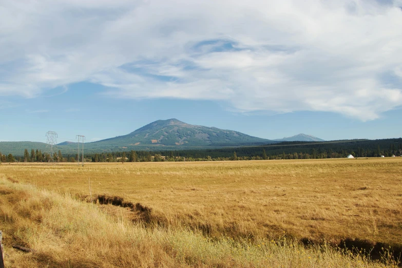 a man riding on the back of a motorcycle down a dirt road, unsplash, land art, mountain behind meadow, oregon, panorama distant view, 2000s photo