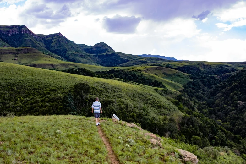 a man standing on top of a lush green hillside, by Peter Churcher, pexels contest winner, zulu, hiking trail, panoramic, annie lebovetz