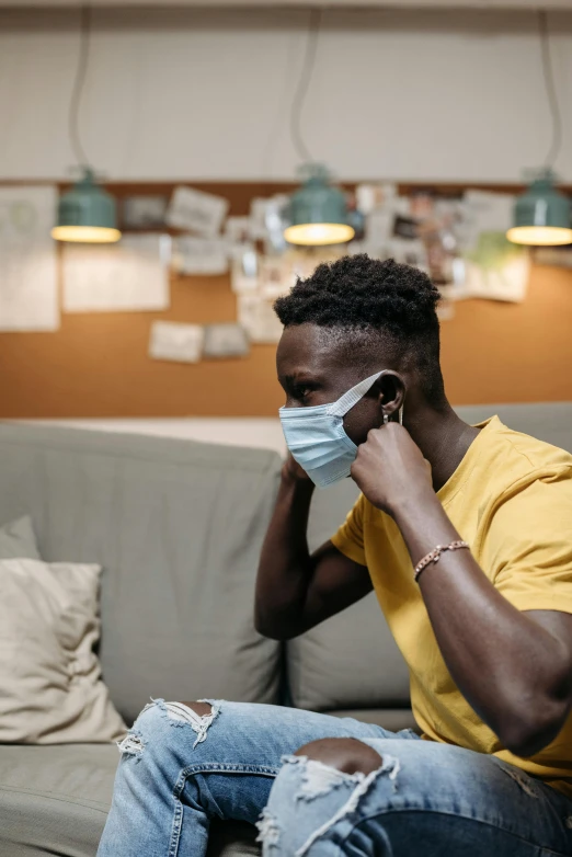 a man sitting on a couch talking on a cell phone, surgical mask covering mouth, black man, 2019 trending photo, heartbreak