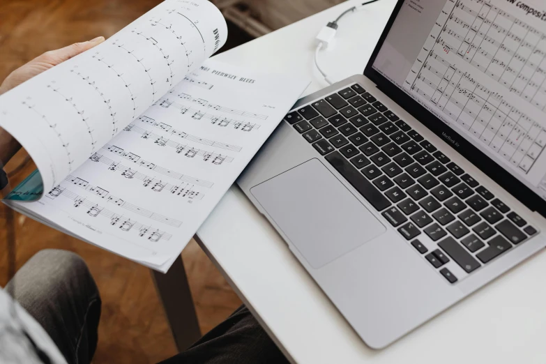 a laptop computer sitting on top of a white table, an album cover, by Julia Pishtar, pexels, sheet music, schematic in a notebook, conductor, creative coder with a computer