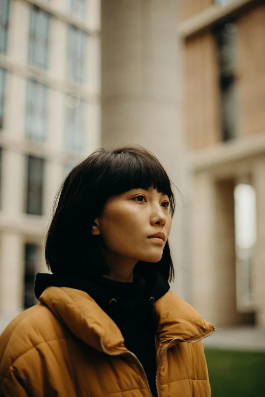 a woman standing in front of a tall building, inspired by helen huang, trending on pexels, visual art, short black hair with bangs, brown jacket, thoughtful expression, ethnicity : japanese