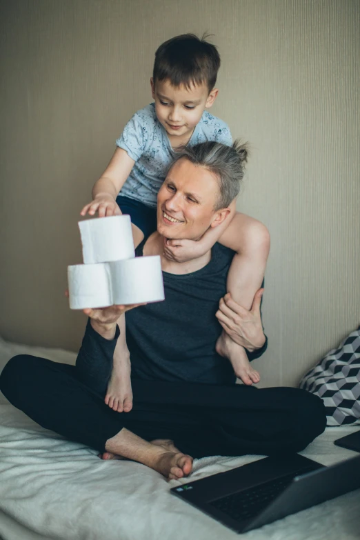 a man sitting on top of a bed holding a child, pexels contest winner, toilet paper, non-binary, square, hexagonal shaped