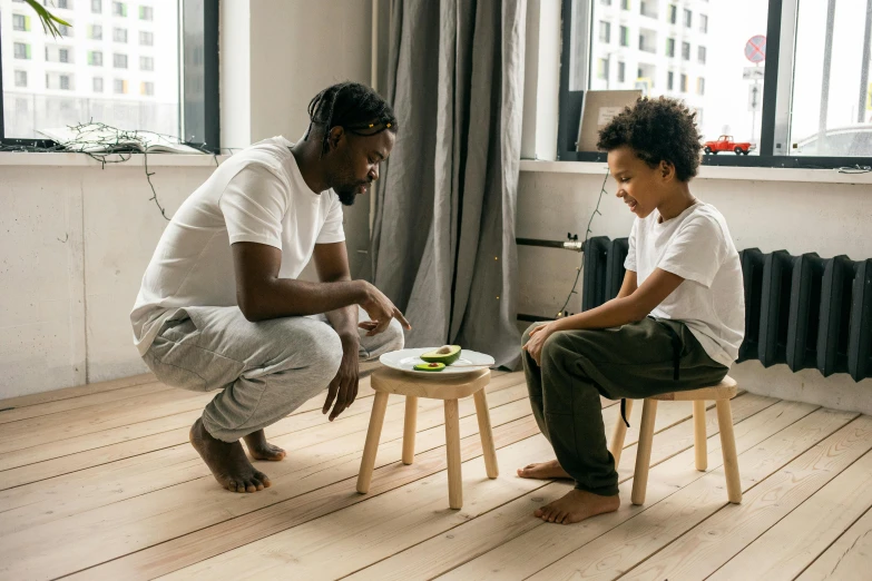 a man sitting on a stool next to a little boy, pexels contest winner, avacado chairs, black man, tapping in to something greater, health