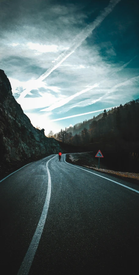 a person standing on the side of a road, by Sebastian Spreng, pexels contest winner, downhill landscape, thumbnail, sports photo, hilly road