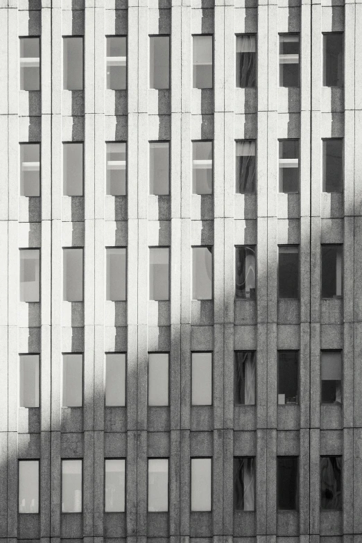 a black and white photo of a tall building, inspired by David Chipperfield, unsplash contest winner, brutalism, windows and walls :5, square shapes, back lit, window ( city )