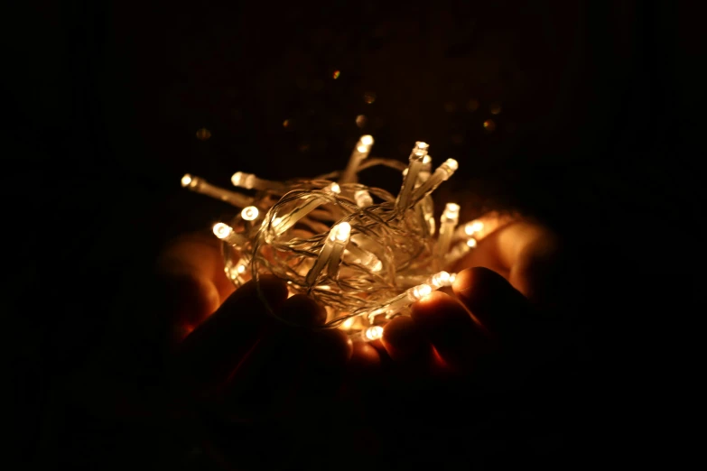 a person holding a string of lights in their hands, inspired by Cornelia Parker, unsplash, light and space, close up photograph, fairy dust, made of glazed, low detailed