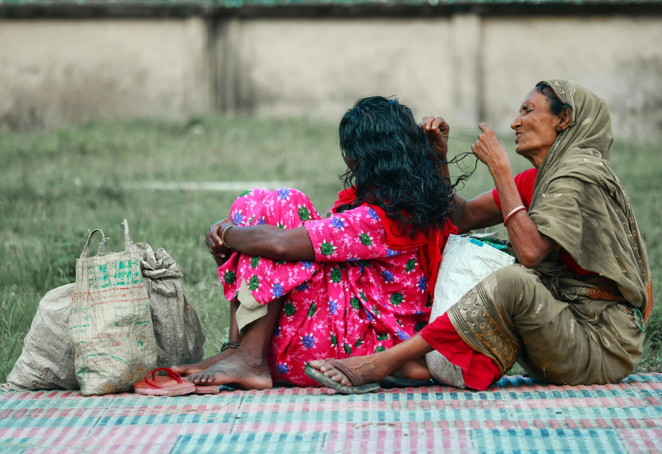 a couple of women sitting on top of a grass covered field, pexels contest winner, streets of calcutta, bags on ground, an old lady with red skin, small