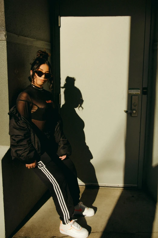 a woman leaning against a wall next to a door, an album cover, inspired by Elsa Bleda, unsplash, realism, man in adidas tracksuit, sunglasses, black habit, cindy avelino