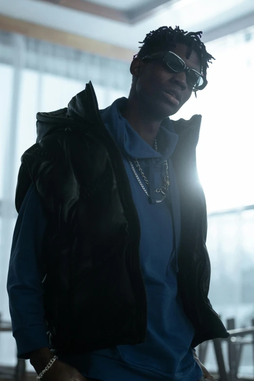 a man in a blue shirt and black jacket, an album cover, inspired by Terrell James, trending on pexels, 2 chainz, moody cinematic lighting, john carmack, model is wearing techtical vest