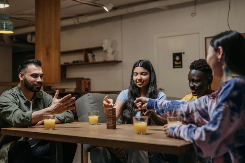 a group of people sitting around a wooden table, pexels contest winner, hurufiyya, avatar image, cardistry, candid photo, holding a drink