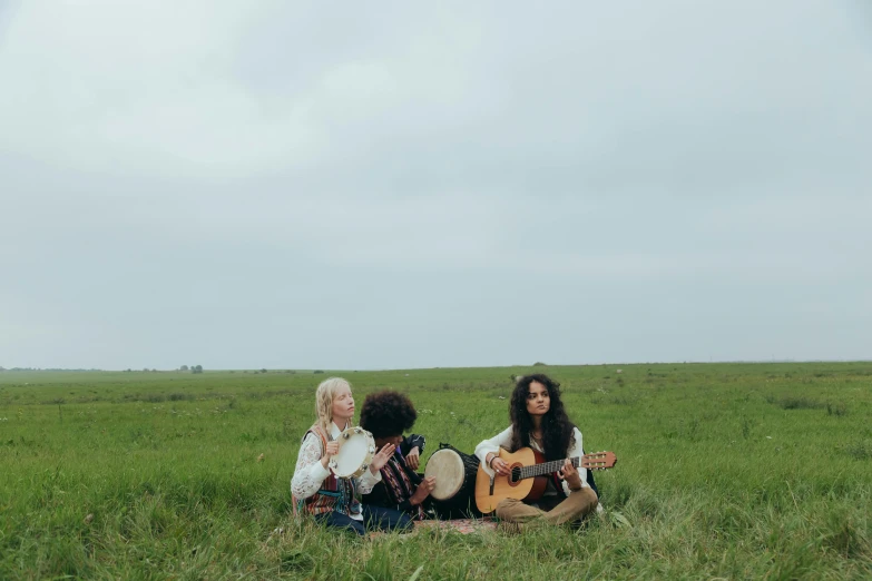 a group of women sitting on top of a lush green field, an album cover, by Winona Nelson, pexels, guitar, white sky, three women, prairie