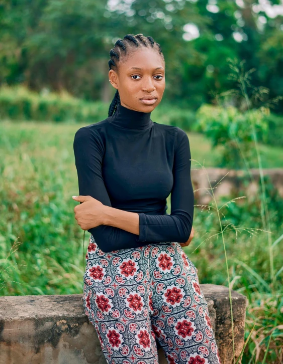 a woman sitting on a wall with her arms crossed, an album cover, inspired by Chinwe Chukwuogo-Roy, trending on unsplash, black turtle neck shirt, standing in a botanical garden, patterned clothing, ((portrait))