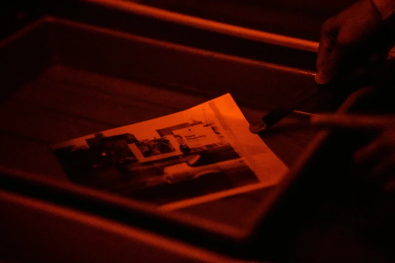 a person cutting a piece of paper with a knife, a picture, by Daniel Lieske, private press, red and orange glow, tabernacle deep focus, on a wooden tray, found film