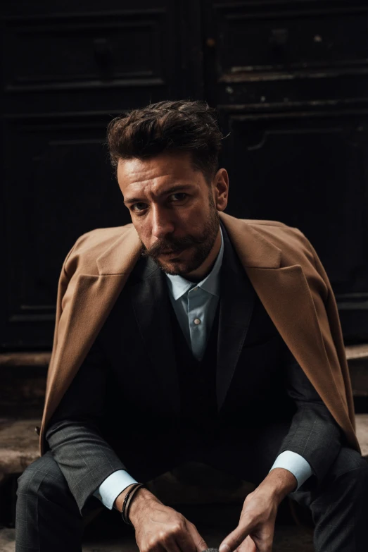 a man sitting on the steps of a building, an album cover, inspired by Francesco Furini, trending on pexels, renaissance, trench coat and suit, hugh jackman portrait, colour photograph, caramel. rugged