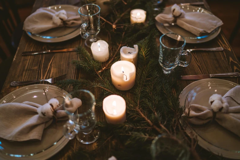 a wooden table topped with plates and candles, by Emma Andijewska, pexels contest winner, evergreen branches, soft warm lighting, casually dressed, recreation