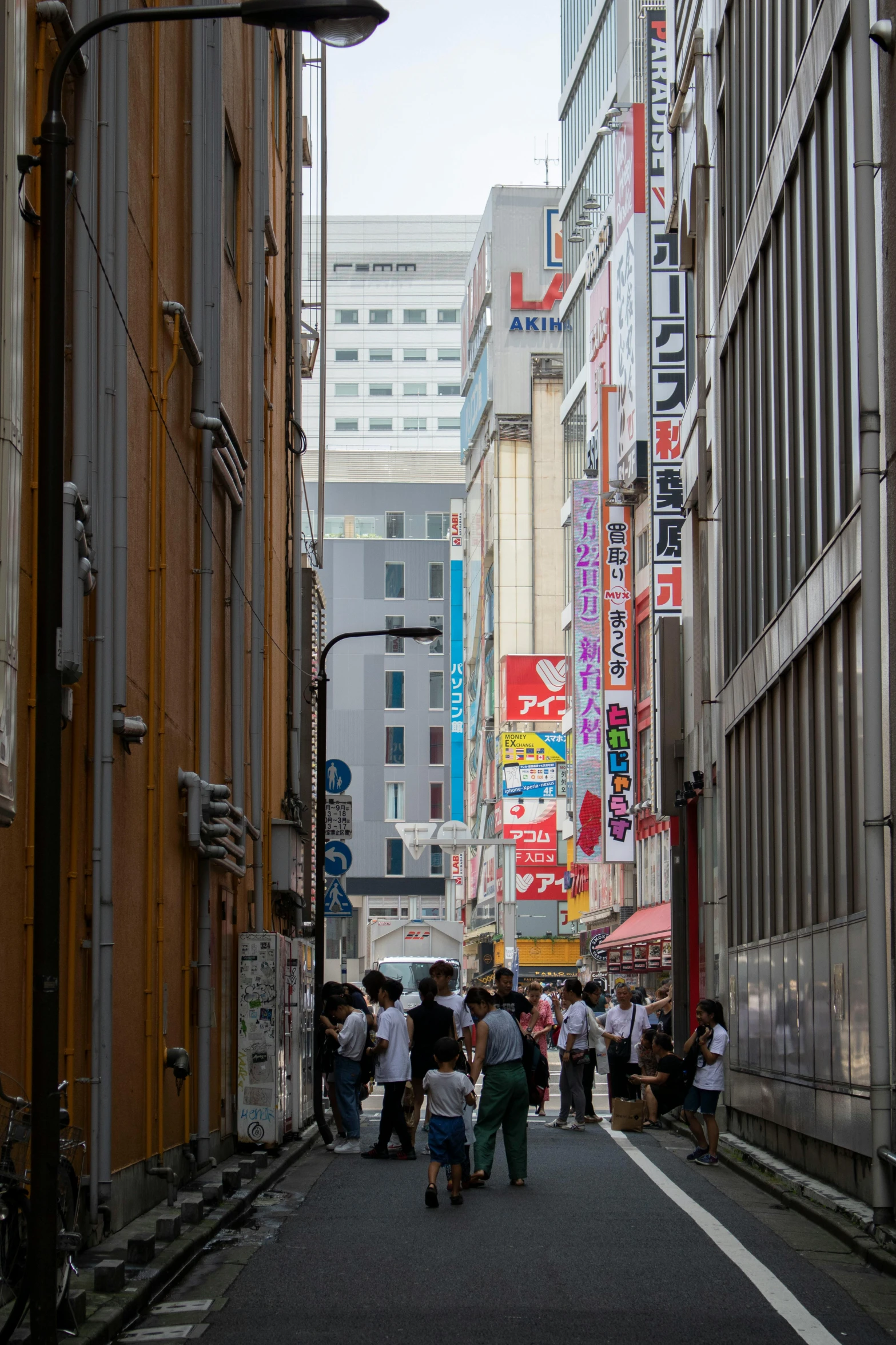 a group of people walking down a street next to tall buildings, a picture, sōsaku hanga, hidden area, city streets, alleyway, street signs